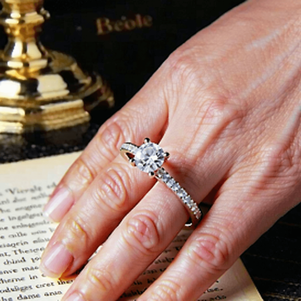 AI Generated Art: "Create a vintage-themed Instagram ad illustrating the sentimental voyage of an engagement ring, from its velvet-box unveiling under the golden gleam of a desk lamp, to its final moment of gentle placement on a lady's hand. Kick off with a close-up view of the ring that underscores its complex jewel patterns and the metal's gentle shimmer. Use smooth, understated panning shots to transition between elements, deepening the nostalgic atmosphere with a faint sepia tone. The sequence should then shift to intertwined hands